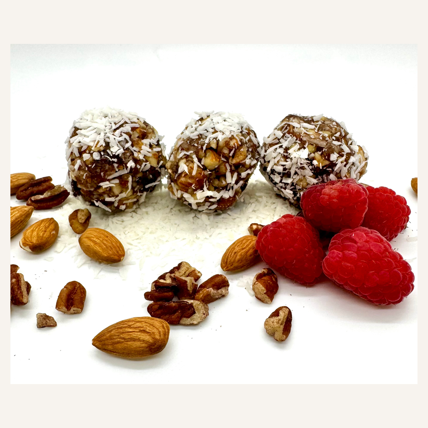 Nuts, raspberries, and coconut-coated balls on a white surface