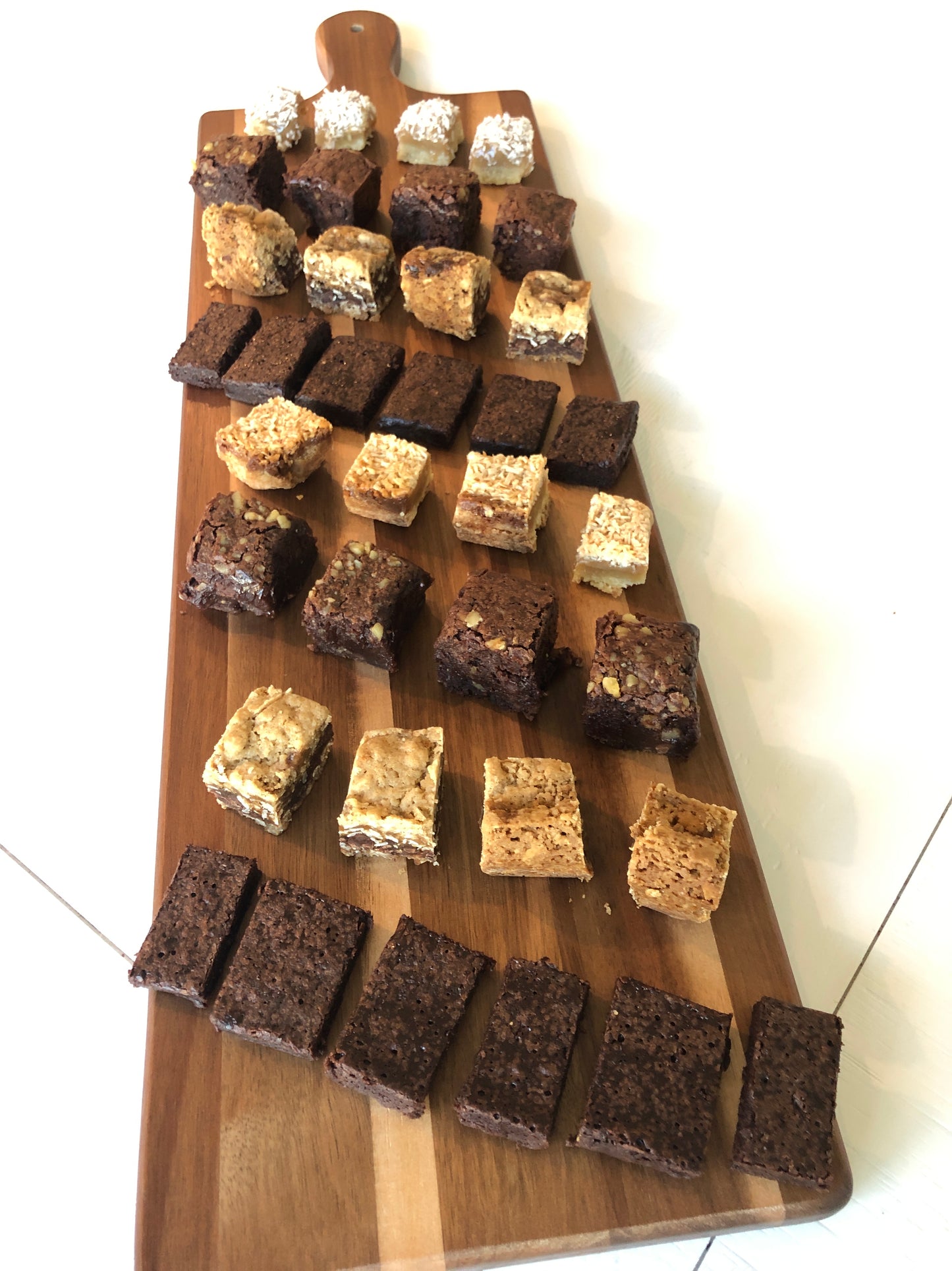 8 bars cut into bites on a bar bite board including brownies, brownie thins, oatmeal caramelitas, and maple coconut gooey bars
