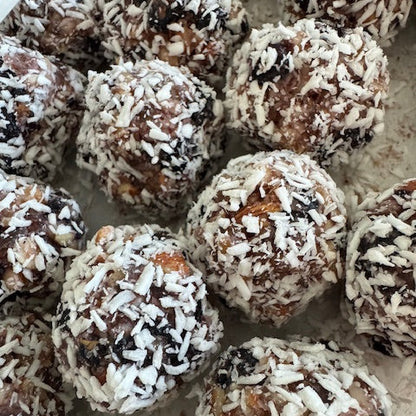 Gluten-free, Dairy-Free and Vegan Lemon Blueberry Coconut Bites made with organic almonds and pecans, sweetened with dates. Three coconut bites displayed with a scattering of dates, almonds, pecans and dried blueberries. 